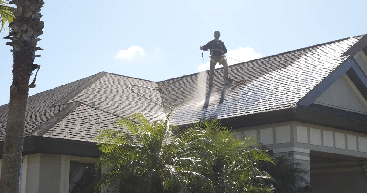 man on top of roof pressure washing