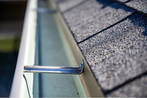 Close-up of clean gutters with hanger bracket secured along the edge of an asphalt shingle roof.