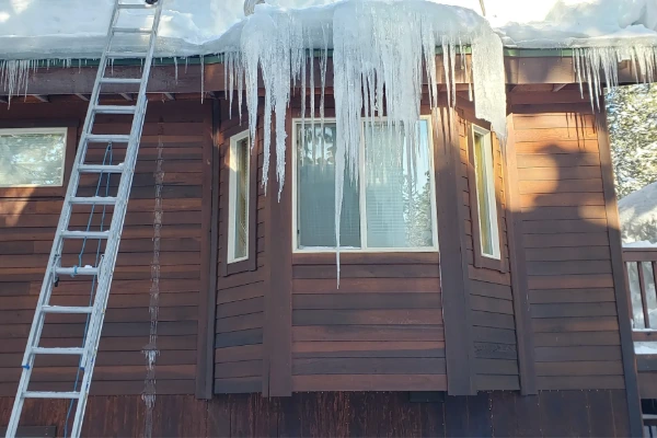 Icicles and ice buildup along a roofline next to a ladder used for ice dam removal.