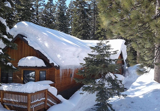 Heavy snow and ice dam buildup with icicles along the eaves of a Tahoe-area cabin roof