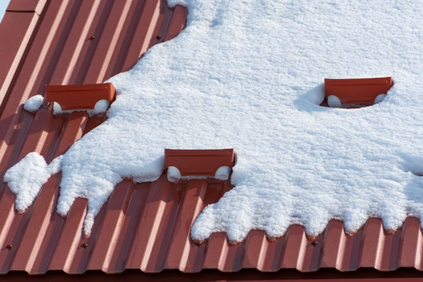 Snow accumulation on a red metal roof with snow guards helping to slow sliding snow and reduce roof load damage.