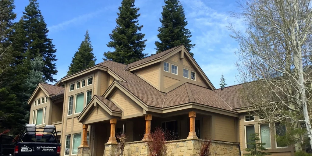 Residential roof with brown asphalt shingles on a large Tahoe-area home in spring, with a Mills Roofing truck parked in the driveway.