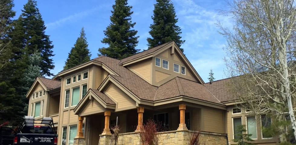 Residential roof with brown asphalt shingles on a large Tahoe-area home in spring, with a Mills Roofing truck parked in the driveway.